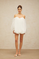Young woman wearing a white layered bubble tulle mini dress with short puffed sleeves standing against a plain background