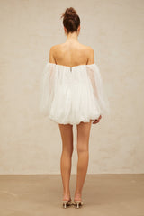 Young woman wearing a white layered bubble tulle mini dress with short sleeves and a flared skirt standing against a plain background