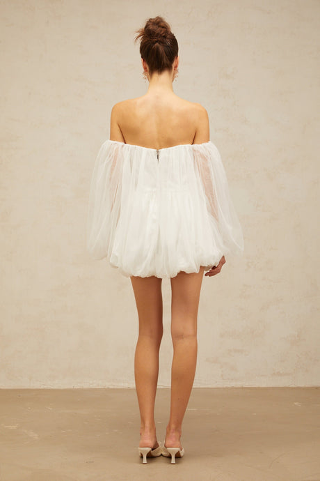 Young woman wearing a white layered bubble tulle mini dress with short sleeves and a flared skirt standing against a plain background