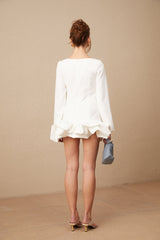 Young woman wearing a white mini dress with a bubble skirt and short puff sleeves standing against a plain background