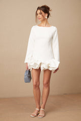 Young woman wearing a white mini dress with a bubble skirt and short sleeves standing against a plain background