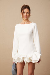 Young woman wearing a white mini dress with a bubble skirt and short sleeves standing against a plain background