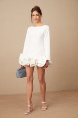 Young woman wearing a white mini dress with a bubble skirt and short sleeves standing against a plain background