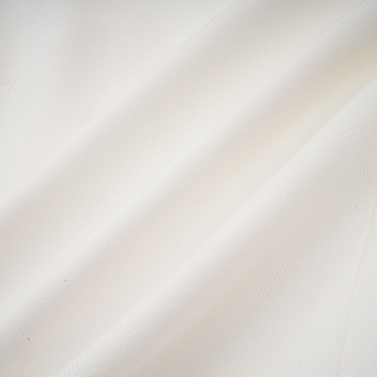 Young woman wearing a white mini dress with a bubble skirt and short sleeves standing against a plain background