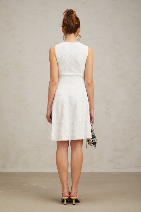 Young woman wearing a white mini dress with a star pattern knitted design and jasmineinspired details