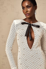 Young woman wearing a white mini dress with cutout details and a decorative bowknot accent standing against a plain background