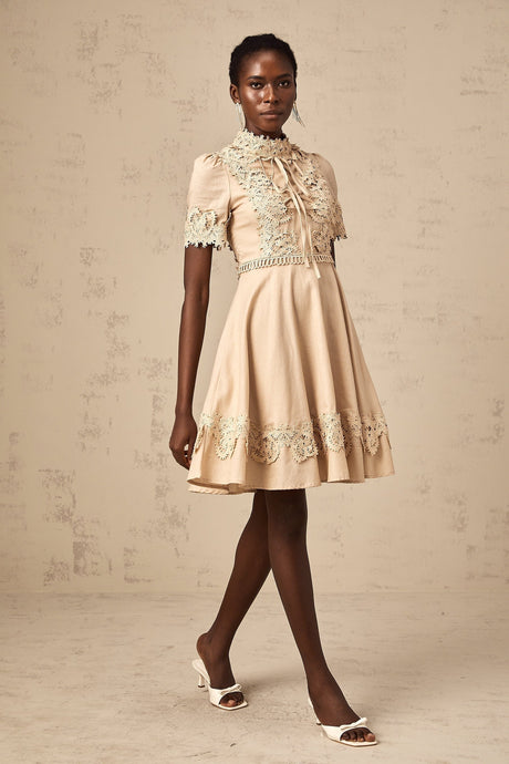 Young woman wearing a white mini dress with flared skirt and corded lace details standing in front of neutral background