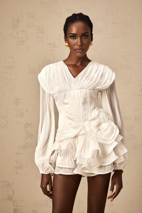 Young woman wearing a white mini dress with full pleating and cinched waist standing in front of neutral background