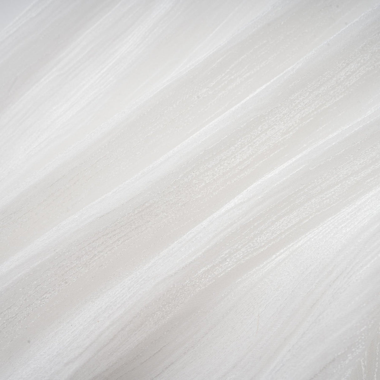 Young woman wearing a white pleated mini dress with cinched waist detail standing against plain background