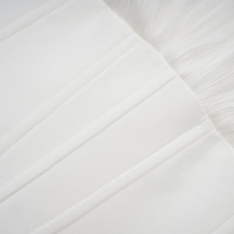 Young woman wearing a white pleated mini dress with cinched waist standing against a plain background