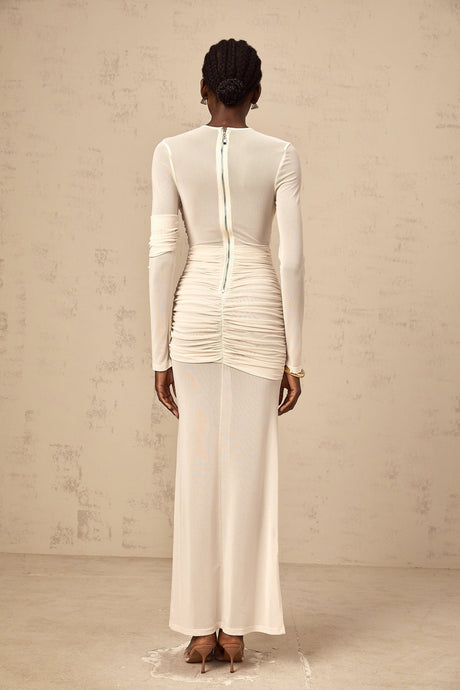 Young woman wearing a white ruched tulle maxi dress with long sleeves and a flowy skirt standing in an elegant pose