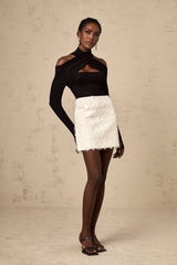 Young woman wearing a white sequined mini skirt standing against a plain background