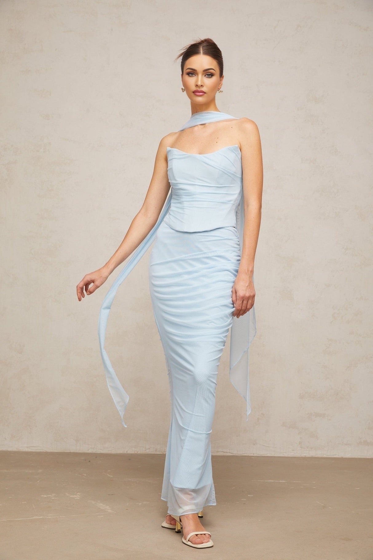 Young woman wearing blue matching set with ruched tulle top and skirt standing against plain background