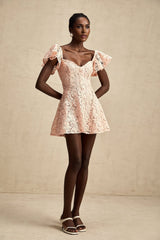 Young woman wearing pink lace mini dress with flutter sleeves posing against plain background
