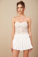 Young woman wearing white lace crop top and matching high waisted skirt standing against plain background