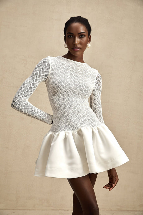 Young woman wearing white lace mini dress with panelled design standing against plain background