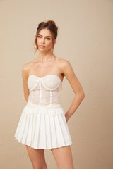 Young woman wearing white lace top and matching skirt set standing against plain background