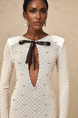 Young woman wearing white mini dress with cutout details and bowknot embellishment standing against plain background