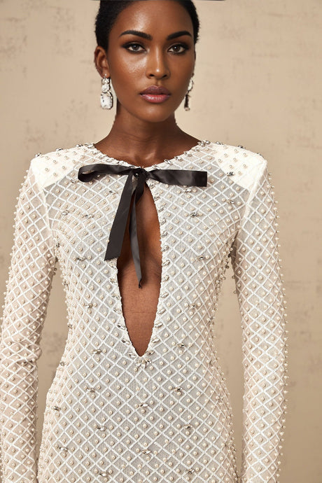 Young woman wearing white mini dress with cutout details and bowknot embellishment standing against plain background