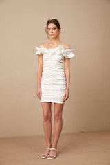 Young woman wearing white offshoulder ruffled mini dress standing against plain background